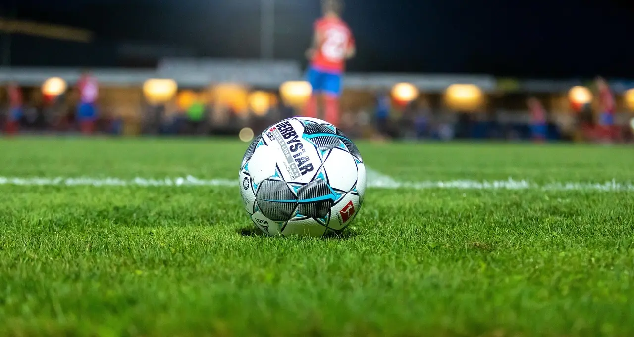Fodbold på græs med stadionlys i baggrunden